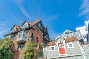 Facade of multi-storey houses in San Francisco, California in a low angle view. There is a house on the left with bricks beside the house with gray vinyl lap sidings and red door on the second floor.