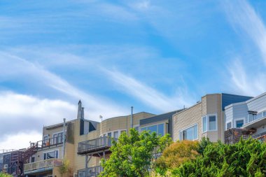 Complex multi-storey residential buildings with wooden wall sidings in San Francisco, California. There are trees on the right and a view of an outdoor staircase at the building on the left.