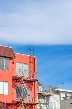 View of an apartment buildings at San Francisco, California with metal emergency staircase outdoors. There is a coral peach building on the left beside the smaller white building on the right.
