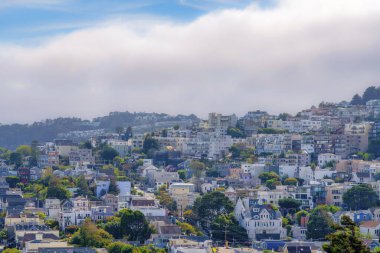 Sloped suburbs of San Francisco, California with large apartment buildings. Residential buildings and a view of electrical posts along the street in the middle.