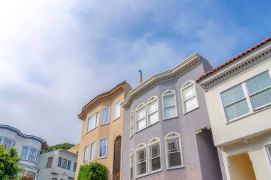 Low angle view of suburbs residences in San Francisco, California. Front exterior of complex houses with ornate trims and different wall colors against the clouds at the sky background.