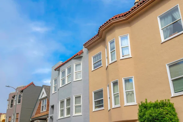 Row of townhouses and single-family home in a low angle view in San Francisco, California. There is a single-family home with gable roof and wood shingles in the middle of taller townhouses.