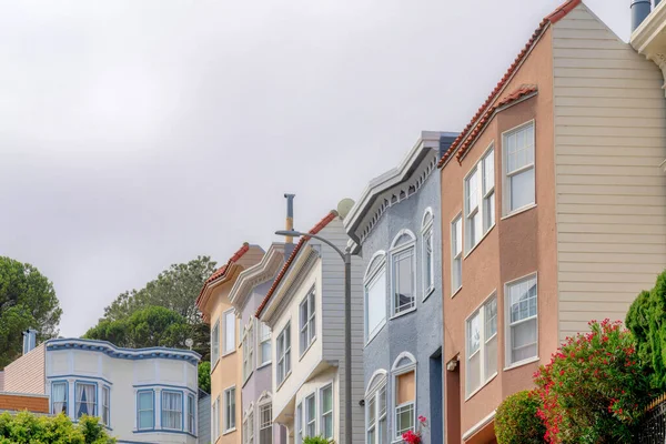 Row of suburban houses in a low angle view at San Francisco, California. There is a street lamp in the middle near the houses and a view of a house with beige and white walls at the backs.