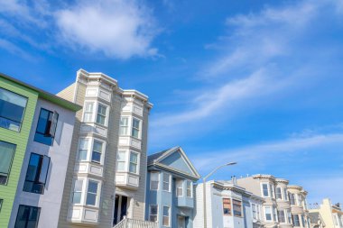 Suburban neighborhood in San Francisco, California with townhomes. Row of residential buildings with different facade structures and a view of sky at the back.