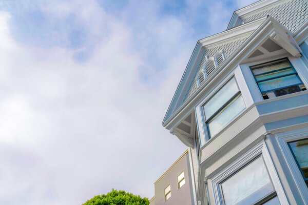 Suburban house in a low angle view with reflective glass windows and scalloped sidings on its peak. Residence exterior in San Francisco, California with a cloudy sky view at the background.