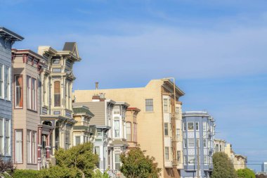 Row of multi-storey residential buildings in San Francisco, California. There are townhouses and apartment buildings in a row with trees at the front.