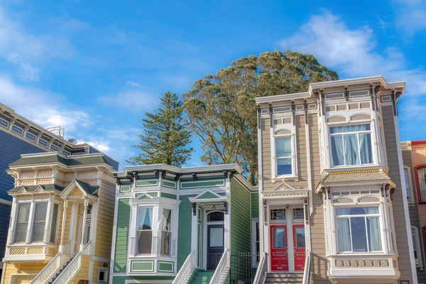 Suburban houses with victorian style exterior in San Francisco, California. There is a beige house on the right with red front doors beside the green house with black door near the yellow house.