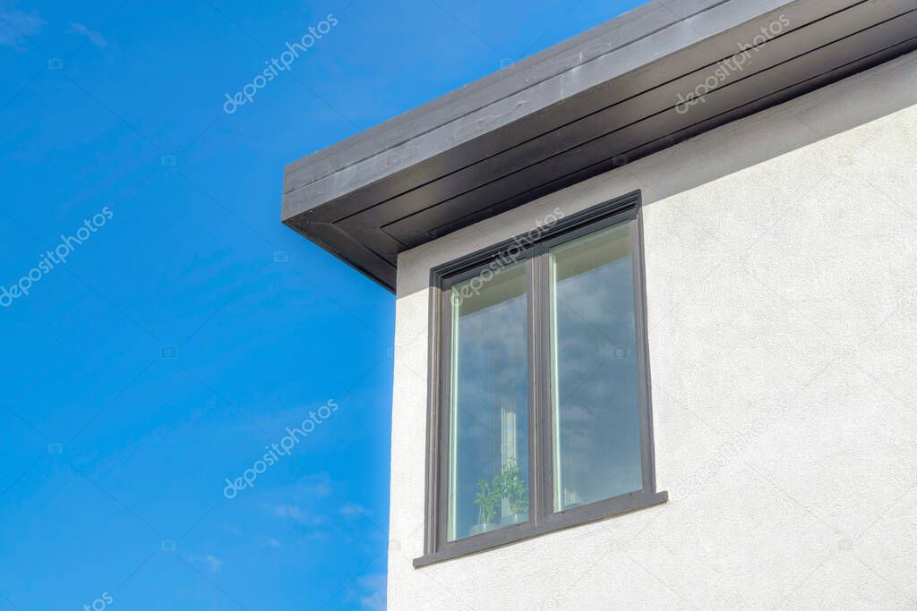 Picture window with clear glass panes and gray frmaes in San Francisco, California. Home exterior with white wall and black wooden celing against the clear sky background.