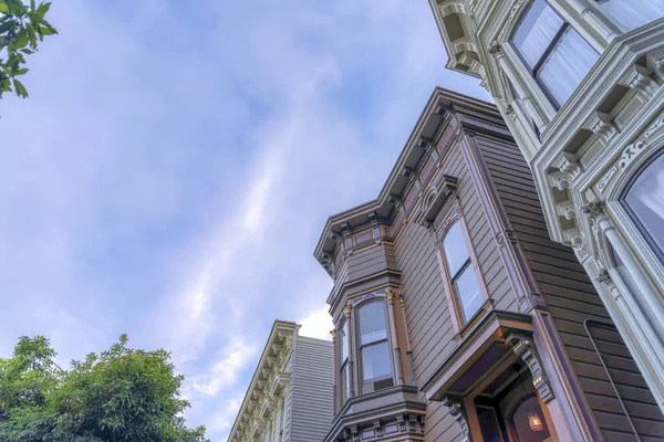 Victorian style townhouse buildings in a low angle view in San Francisco, California. There is a townhouse in the middle with purple exterior and single hung windows.