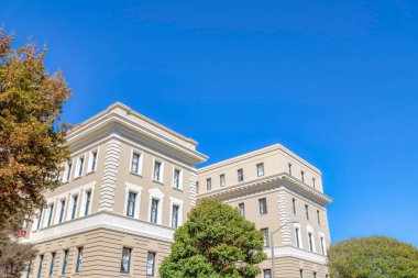 Apartment buildings with georgian style exterior against the blue sky in San Francisco, California. Two multi-storey apartment buildings with beige painted exterior and trees outdoors.