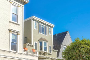 Close-up of second floor exterior of houses in San Francisco, California. There is a house with sage green sidings in the middle near the white house on the left and gray house on the right.