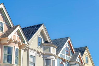 Second-floor close-up of complex houses in San Francisco, California. There are houses with decorative grids on the roof peaks and there is a house with sunburst decor on the right.