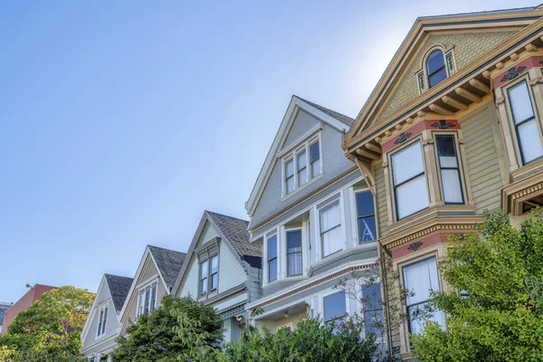 Slanted low angle view of houses with decorative shingles and bay windows at San Francisco, CA. There are two three-storey houses on the right beside the three two-storey houses on the left.