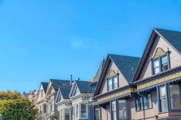 Row of townhouses with decorative exterior in San Francisco, California. Side view of victorian houses with decorative frieze boards and roofs with asphalt composite shingles against the clear sky.