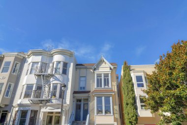 Front exterior of row houses in San Francisco, California. There are townhouses on the left with white exterior and emergency stairs outside beside the townhouse on the right with two front doors.