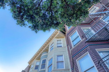 Residential buildings in a low angle view at San Francisco, California with wood shingle sidings. There is a red violet building on the right with emergency stairs near the beige building on the left.