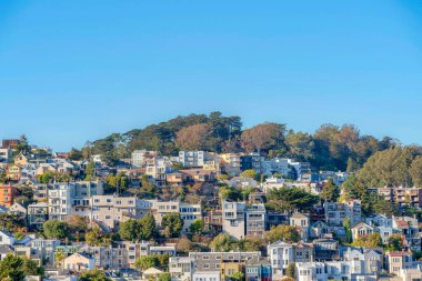 Different residential building structures on a slope of a moountain at San Francisco, CA. There are apartment buildings and townhouses with electrical posts outside.