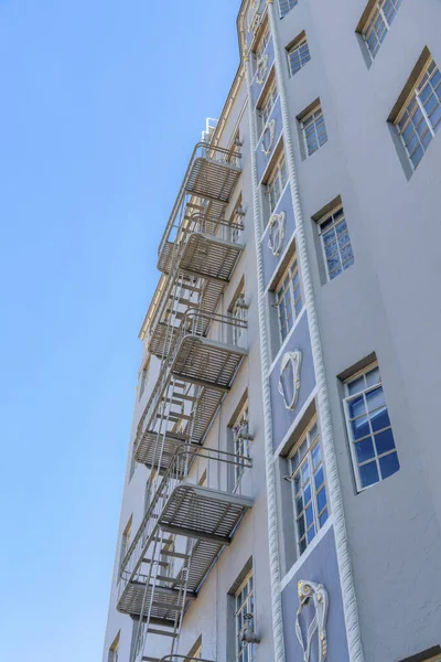 Low angle view of a multi-storey apartment with ornamental wall display and decorative beading. Apartment building with casement windows and emergency staircase.