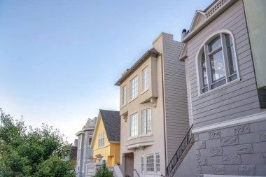 Different home exteriors in San Francisco, California against the sunset sky background. There are two houses on the right with railings at the doorsteps near the yellow house in the middle.