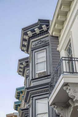 Close-up of victorian style homes with decorative brackets in San Francisco, California. There is a white house at the front and railings with brackets below beside the house with gray wood siding.