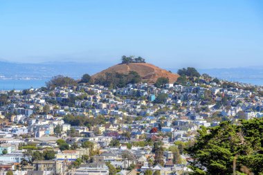 Dense houses near the hill in the middle against the bay view in San Francisco, California. High angle view of a residential area near the water against the blue sky at the back.