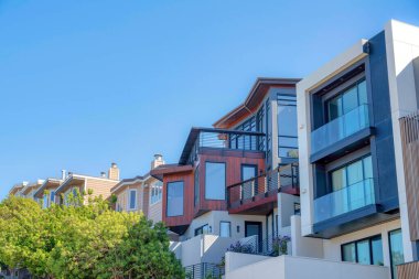 Modern and traditional townhouses in a sloped suburbs of San Francisco, CA. There are two modern townhouses on the right with tall windows and balconies near the traditional townhouses at the back.