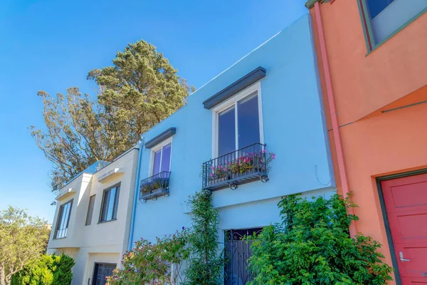 Small houses in the neighborhood in San Francisco, California with painted walls. There is a house on the left with beige wall beside the house in the middle with railings and planters on the window.