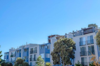 Rows of apartment buildings on a slope in San Francisco, California. There is an apartment building at the front with sliding glass door on its balconies and buildings at the back with glass railings.