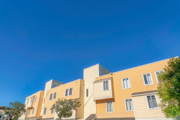 Exterior of an apartment building with beige and yellow wood lap siding in San Francisco, California. Apartment in a low angle view with casement windows and trees at the front.