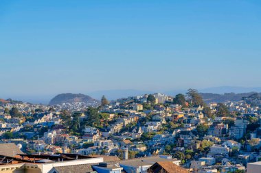 Suburbs of San Francisco, California near the hills and mountains in a high angle view. There is a view of dense residential buildings below against the sky.