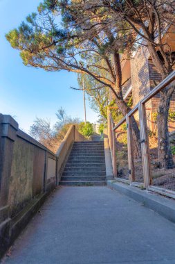 Pathway leading to a stairs outside the fence of a building in San Francisco, California. Concrete path with wall on the left across the fence on the right near the trees and residence building.