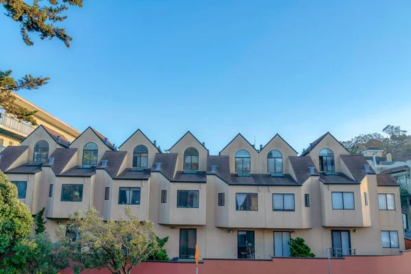 Apartment building with dormer roofs and sliding glass doors in San Francisco, California. Facade of an apartment with sliding windows and brown shingle roofs against the clear sky at the back.