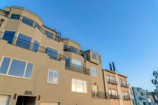 Low angle view of an apartment building with reflective windows and balconies in San Francisco, CA. Large residential house building along with the townhouses on the right with window railings.