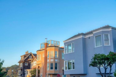 Large residential house buildings near the street lamps and stop sign in San Francisco, California. There are houses with wood shingle siding, roof deck, and picture windows against the clear sky.