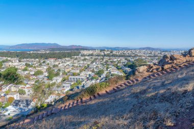 Stairs hiking trail with overlooking view of dense residential buildings at San Francisco, CA. Steps on a slope of a mountain with a view of the town near the mountains and ocean at the back.