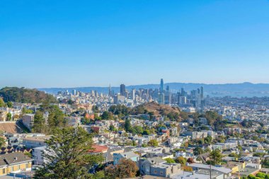 Residential area near the hills against the skyscraper buildings in San Francisco, California. There is a dense houses at the front and a view of commercial buildings at the back near the bay.