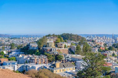 View of a hillside residences from a mountain near the downtown San Francisco, CA. There are residences at the front near the hill with houses against the downtown near the bay at the back.