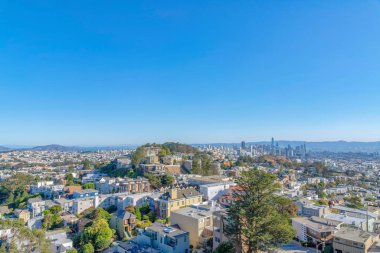 Dense apartment buildings and townhouses around the hill in the middle at San Francisco, CA. High angle view of residential and financial area with skycraper buildings at the back near the bay.