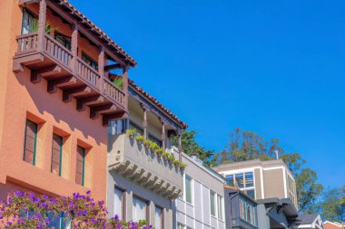 Low angle view of rowhouses with mediterranean and traditional designs in San Francisco, CA. There are two houses on the left with balconies along with the other houses with picture windows.