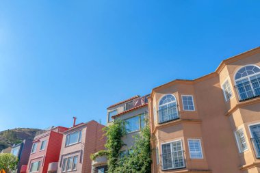 Low angle view of rowhouses in San Francisco, California. There is a house on the left with railings beside the house with crawling plants on the wall near the houses with picture windows on the left.