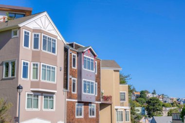 Row of four-storey houses with brown color scheme exterior at San Francisco, California. Three houses at the front of the neighborhood background with a house in the middle with wood shingle sidings.