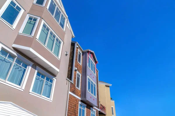 View of houses\' exterior from below against the clear blue sky in San Francisco, CA. There is a house on the left with light brown walls and casement windows beside the house with wood shingle siding.