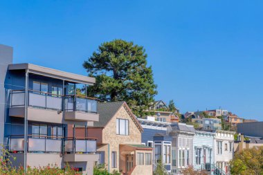 Houses with different exterior in San Francisco, California. There is a house on the left with glass on its balconies beside the house with stone walls along with the other houses with wood sidings.