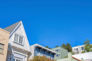 Facade top view of houses in San Francisco, California. Top part exterior of houses with gable and flat roofs against the clear blue sky background.