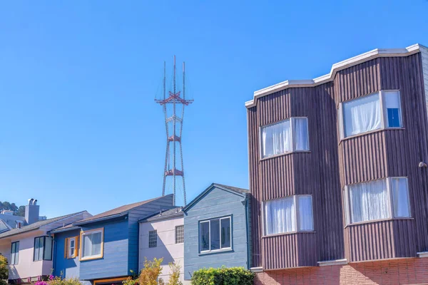 Sutro Tower behind the suburban houses at San Francisco, California. There is a house on the left with four bay windows along with the smaller houses with painted exteriors.