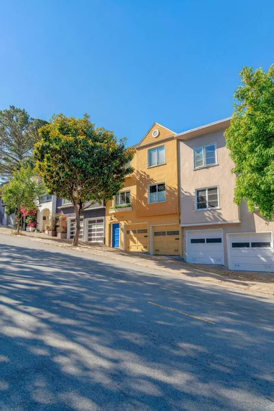 Steep street with houses on the side at San Francisco, California. There is a sloped street at the front of the houses with attached garage and small trees at the front.