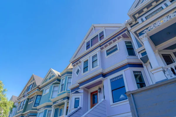 Rowhouses with victorian style exterior in San Francisco, CA. View from below of the houses with painted wood sidings and decorative entrance exterior against the clear sky background.