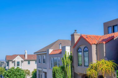 Sloped row of houses against the clear sky background at San Francisco, California. There is a mediterranean style house on the right with cactus at the front.