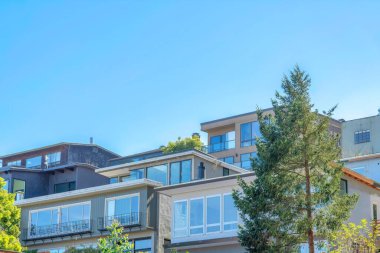 Facade of upper middle class residences in San Francisco, CA. Large house buildings with floor to ceiling picture windows and glass balcony railings against the clear sky.