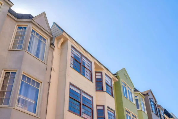 Adjacent houses with paned windows at San Francisco, California. Low angle view of houses with painted stucco walls against the clear blue sky background.